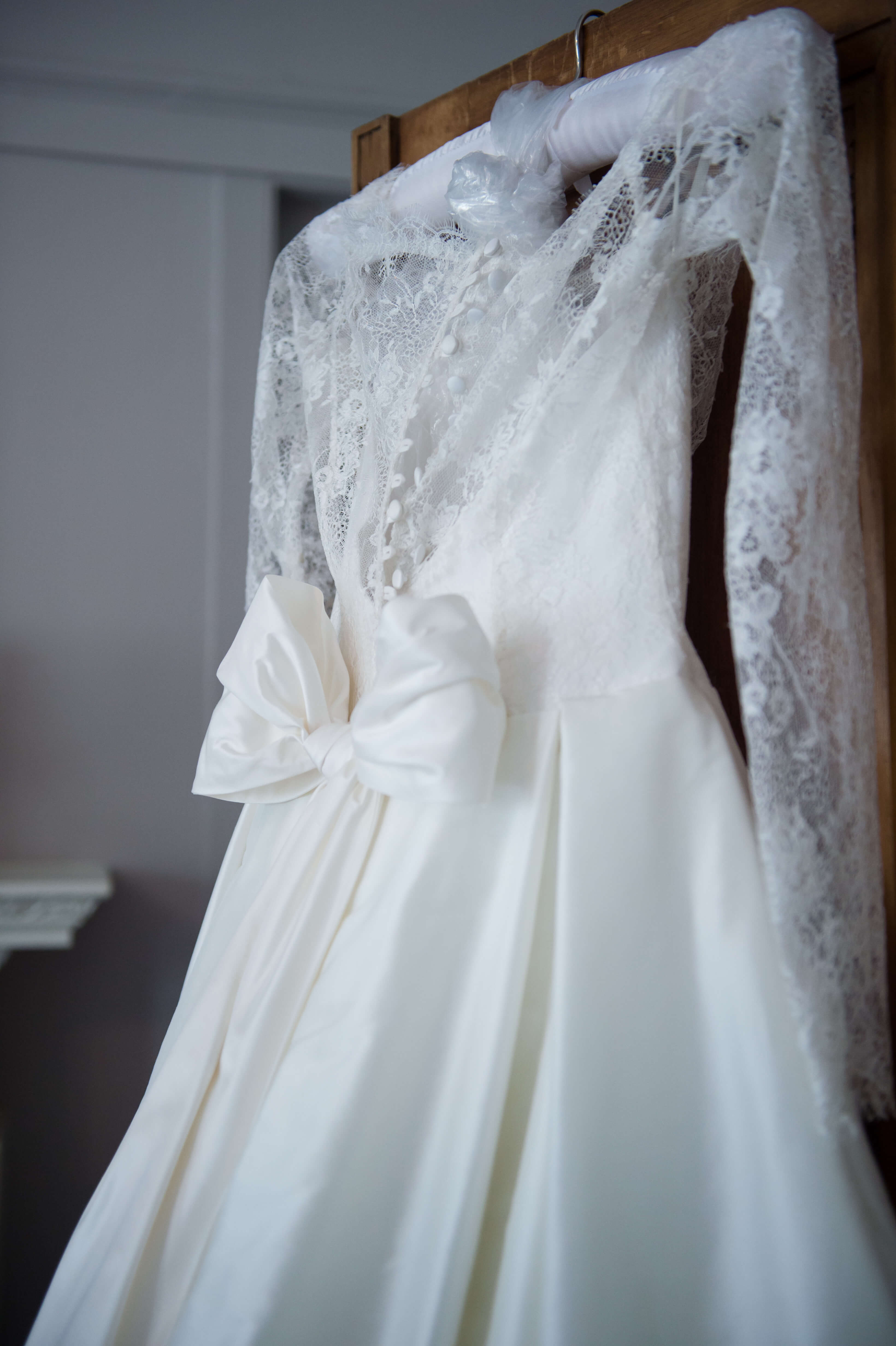 lace wedding gown with a bow hanging on a wardrobe